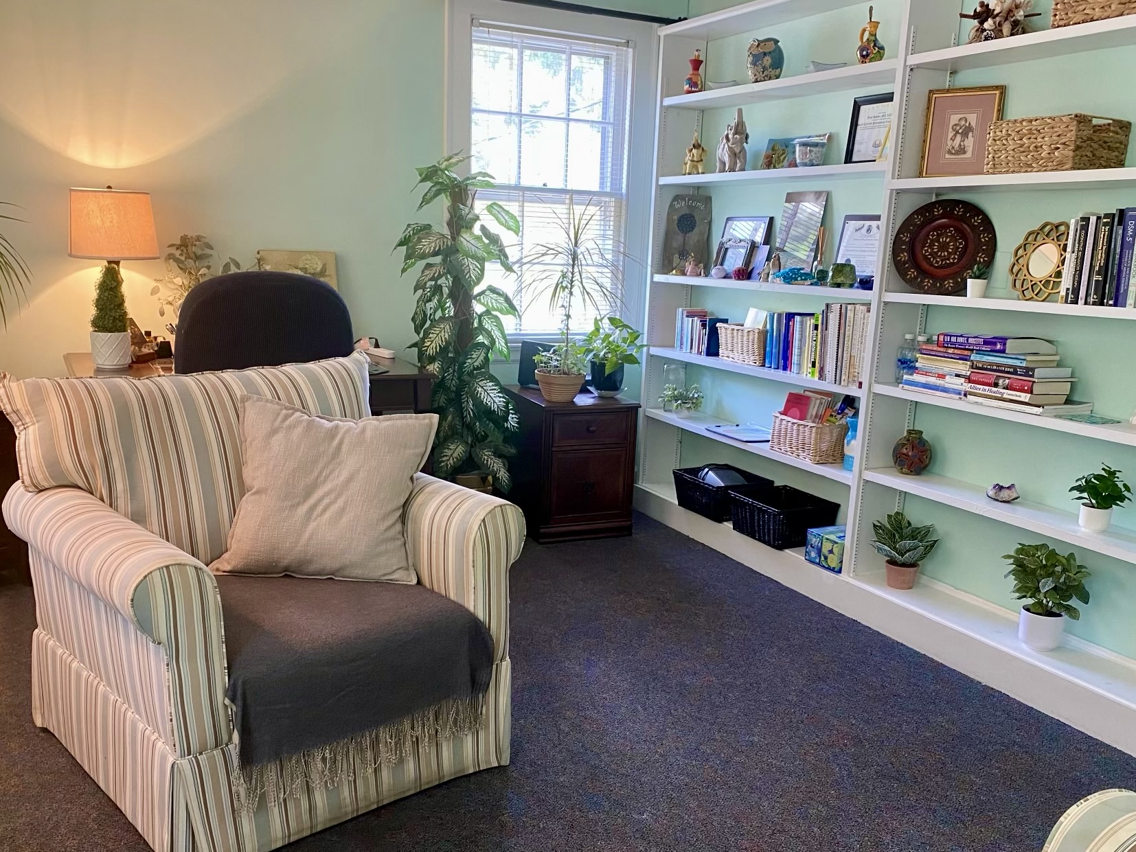 The Reflections Counseling office: a striped armchair beside a sunlit window, surrounded by houseplants and shelves of therapy references